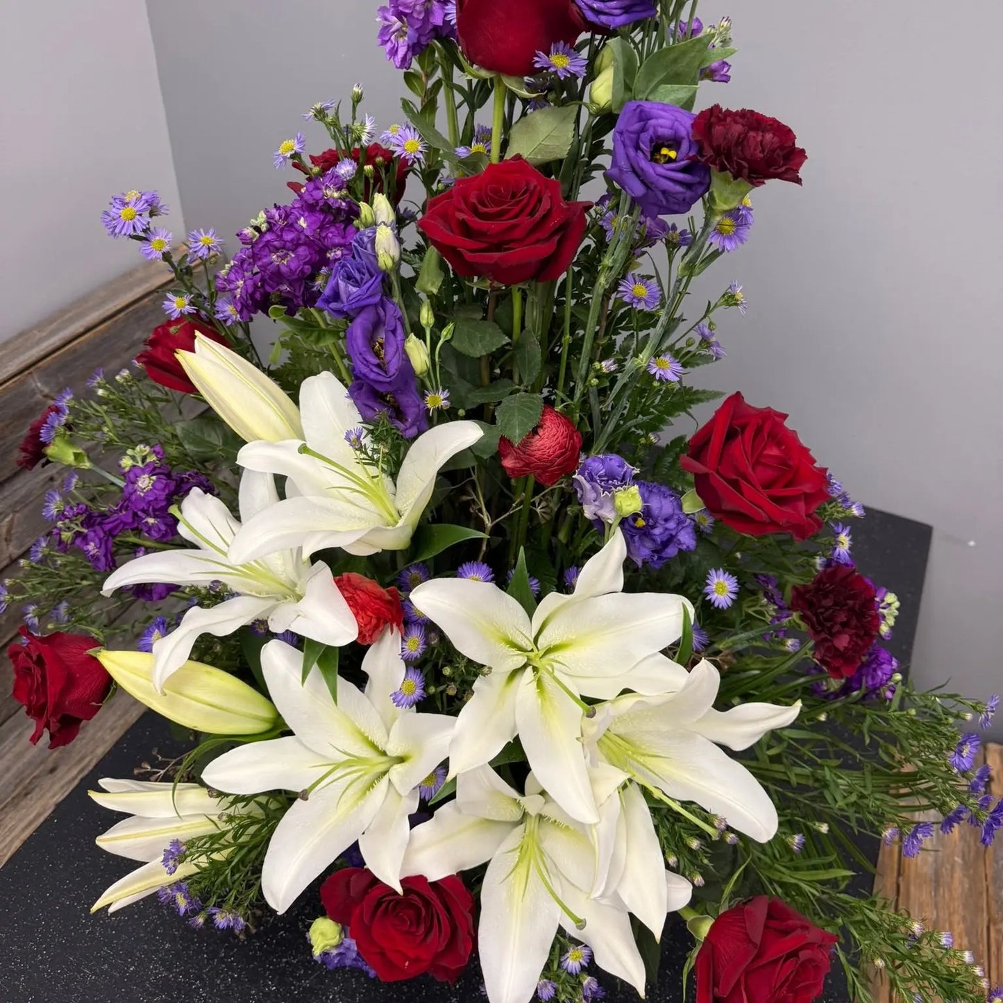 Bouquet of flowers with white lilies, red roses, and purple flowers on a dark surface.