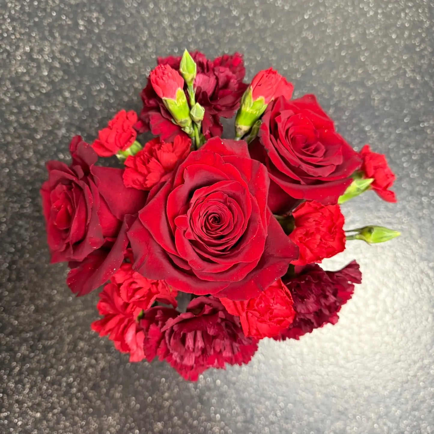 Bouquet of red roses and red carnations on a reflective surface
