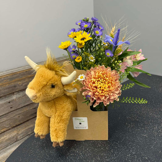 Floral arrangement with a plush toy on a dark surface against a gray wall.