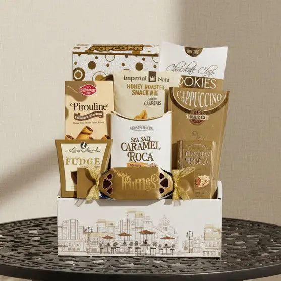 A gourmet gift basket filled with assorted chocolates, snacks, and treats, including Imperial Nuts Cashews, Siete Sal Caramel Roca, and various cookies, arranged in a white and gold cityscape-themed box.