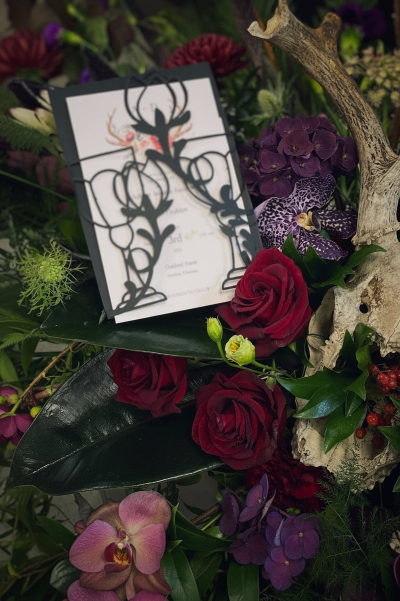 Decorative wedding invitation with antlers surrounded by flowers and antlers