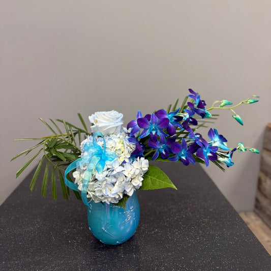 Blue vase with flowers on a dark surface against a gray wall