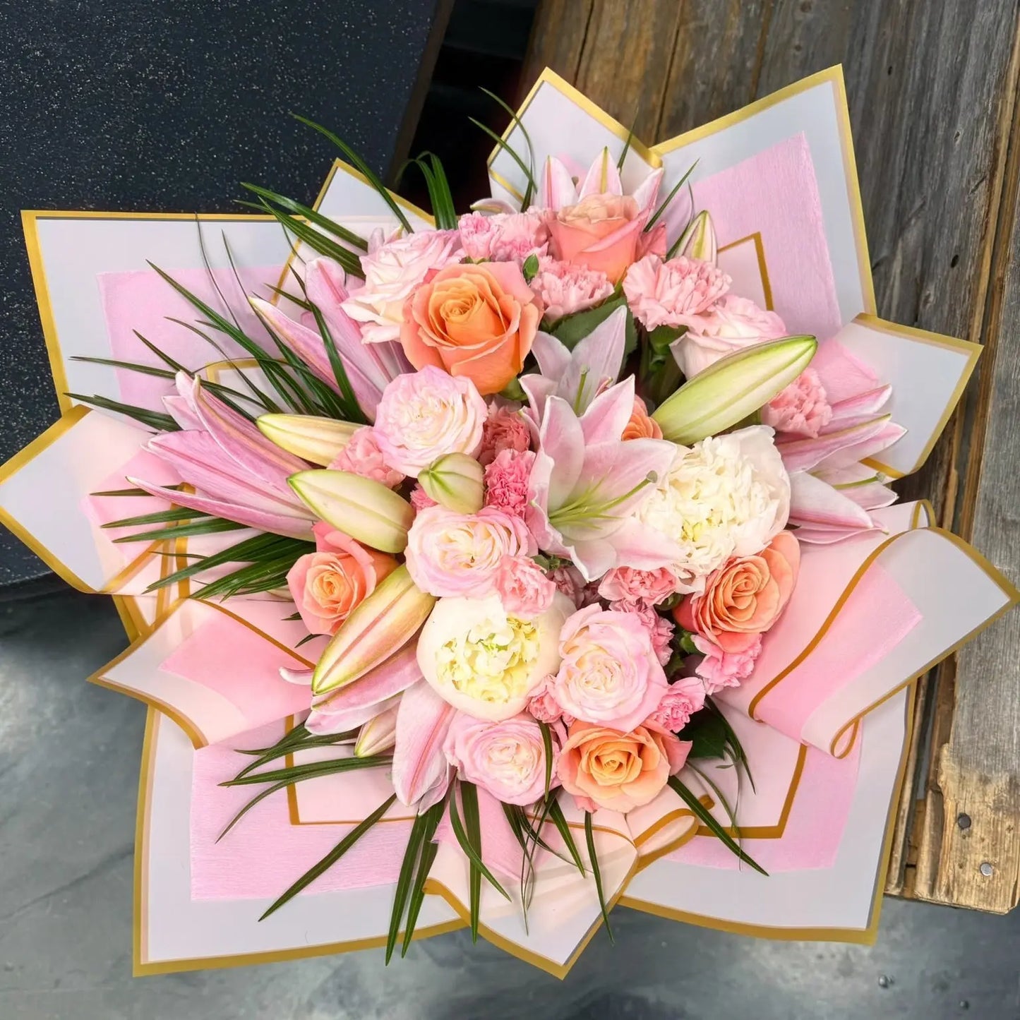 Bouquet of pink and peach flowers in a decorative box on a concrete floor.