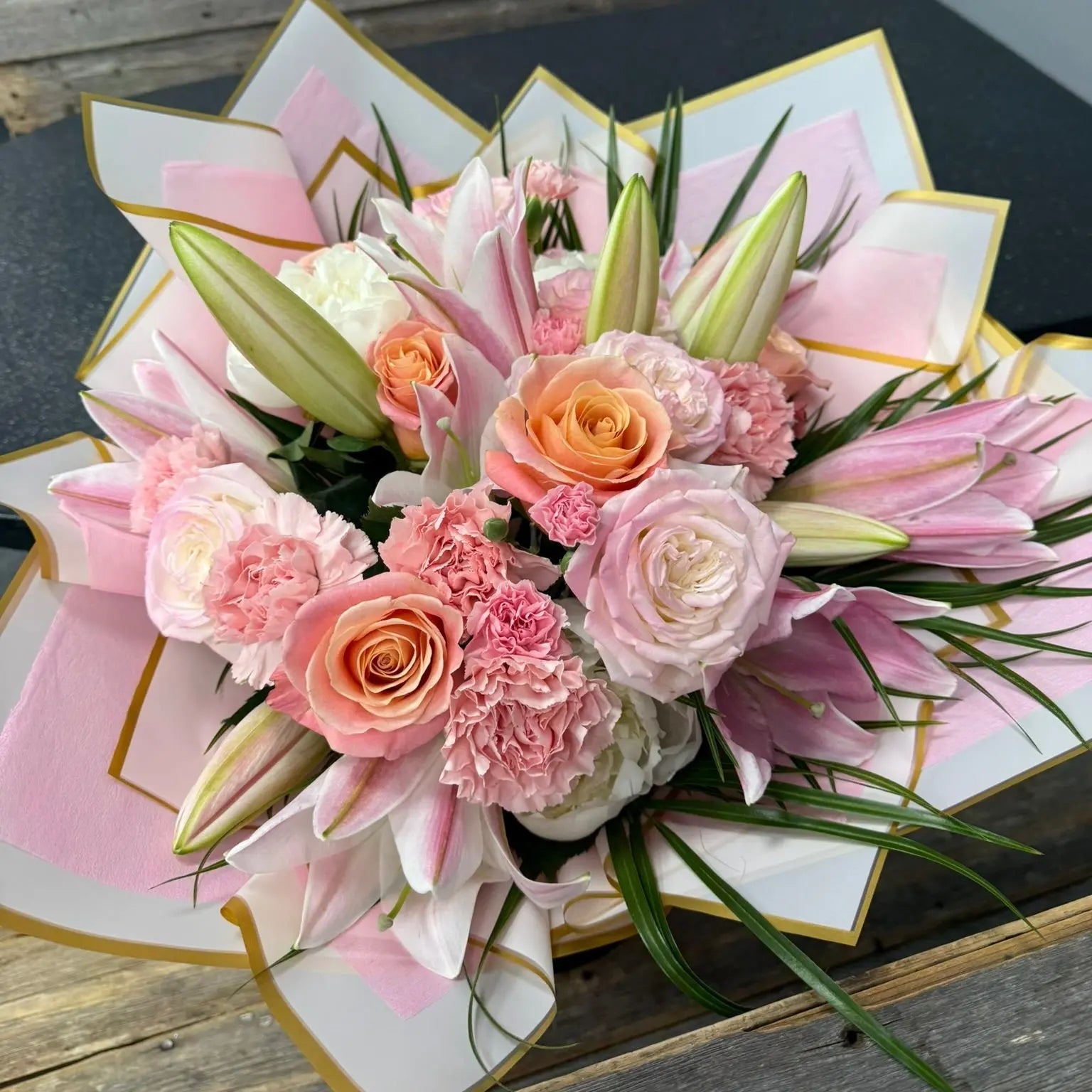 Bouquet of pink and orange flowers in a decorative box on a wooden surface.