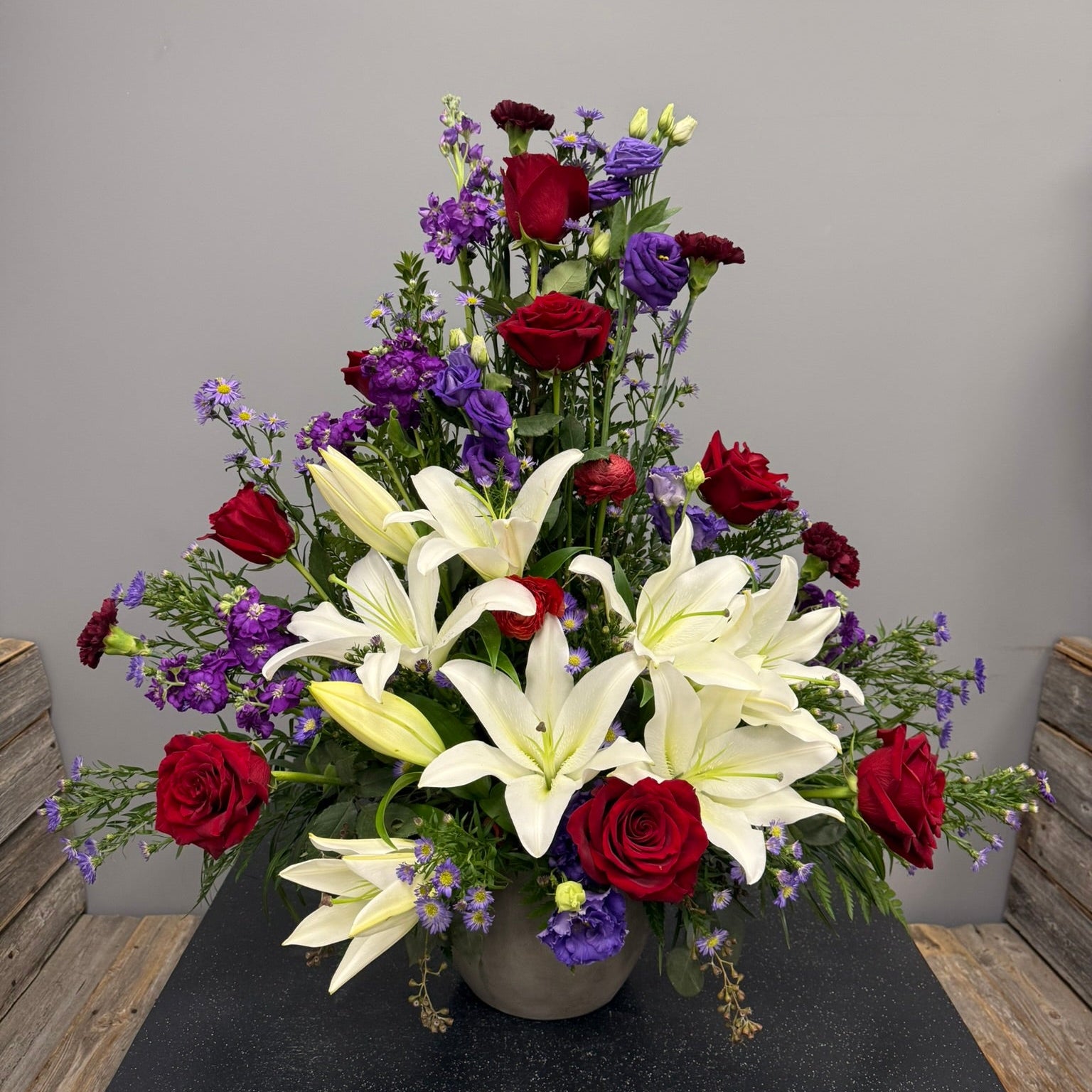 Bouquet of flowers with red roses, white lilies, and purple flowers in a vase on a gray surface.