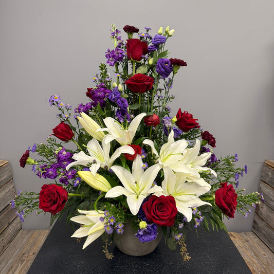 Bouquet of flowers with red roses, white lilies, and purple flowers in a vase on a gray surface.