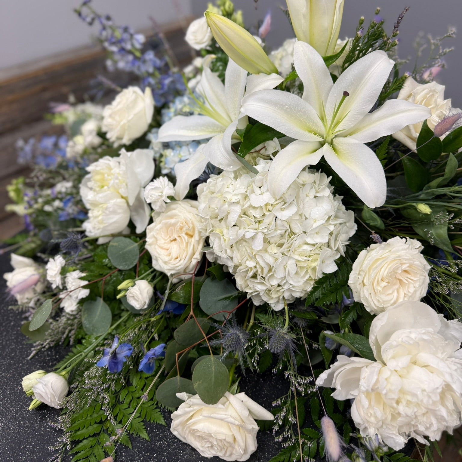 Bouquet of white lilies and roses with greenery on a dark surface.