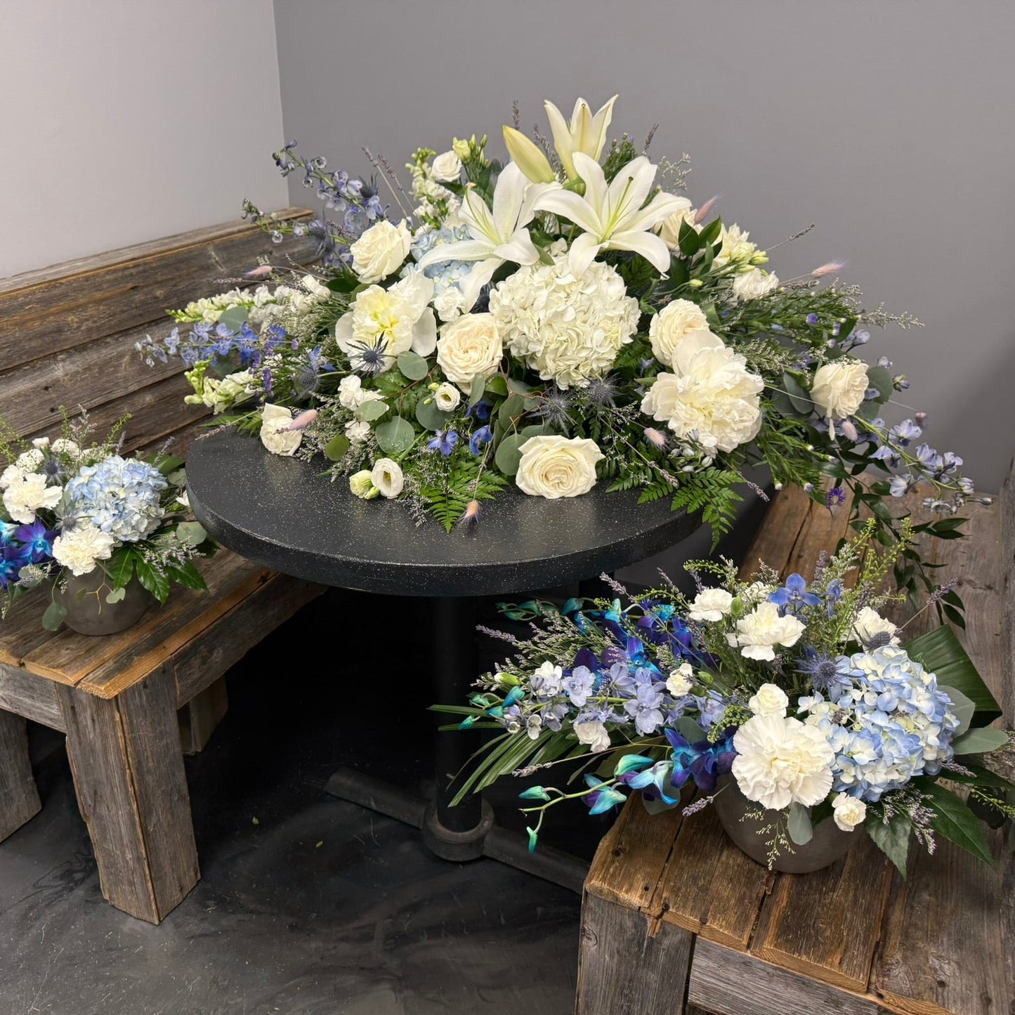 Floral arrangements on a table and benches against a gray wall.