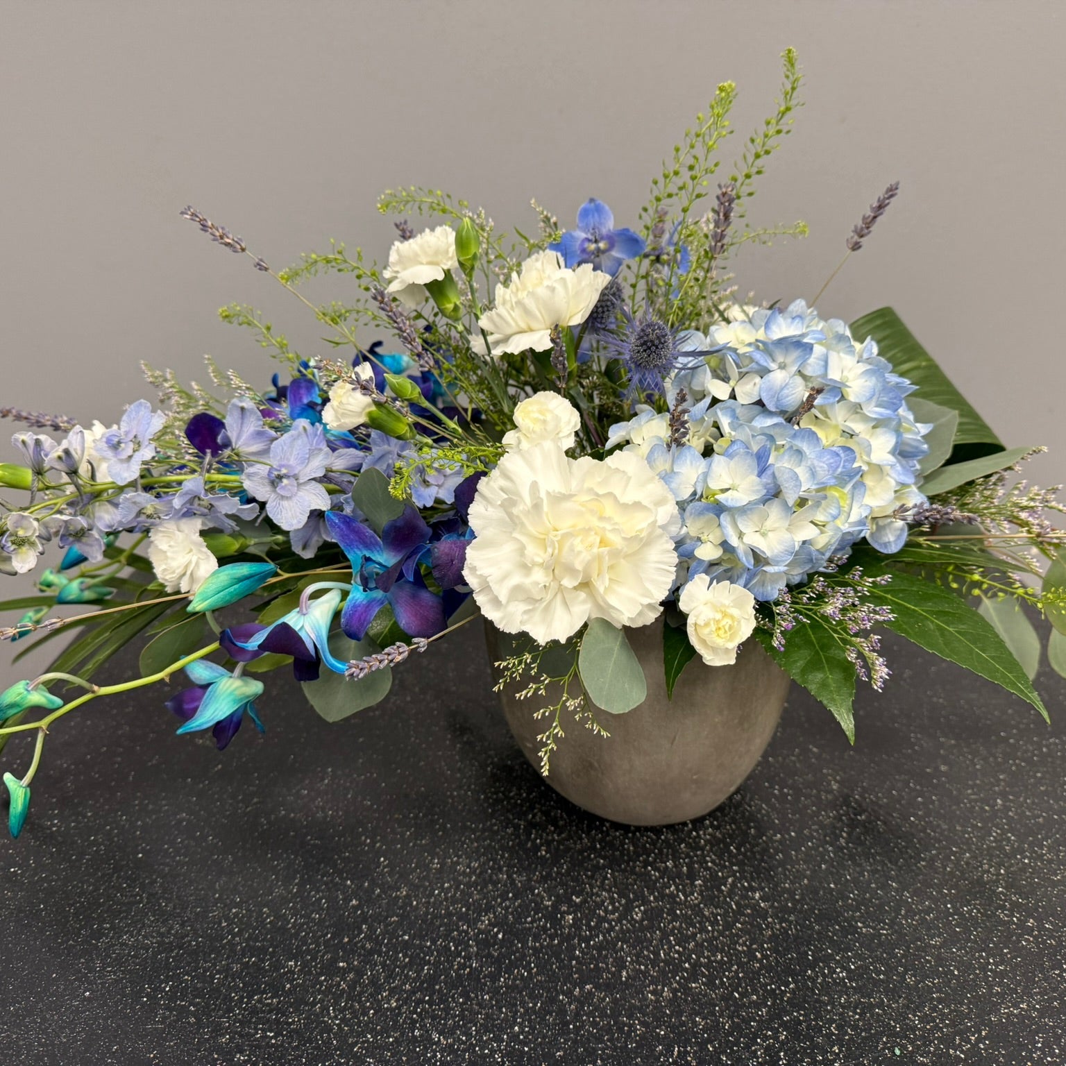 Floral arrangement in a gray vase on a dark surface with a neutral background