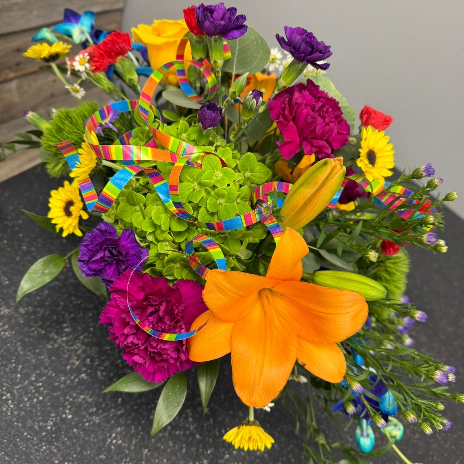 Colorful bouquet of flowers with a rainbow ribbon on a dark surface