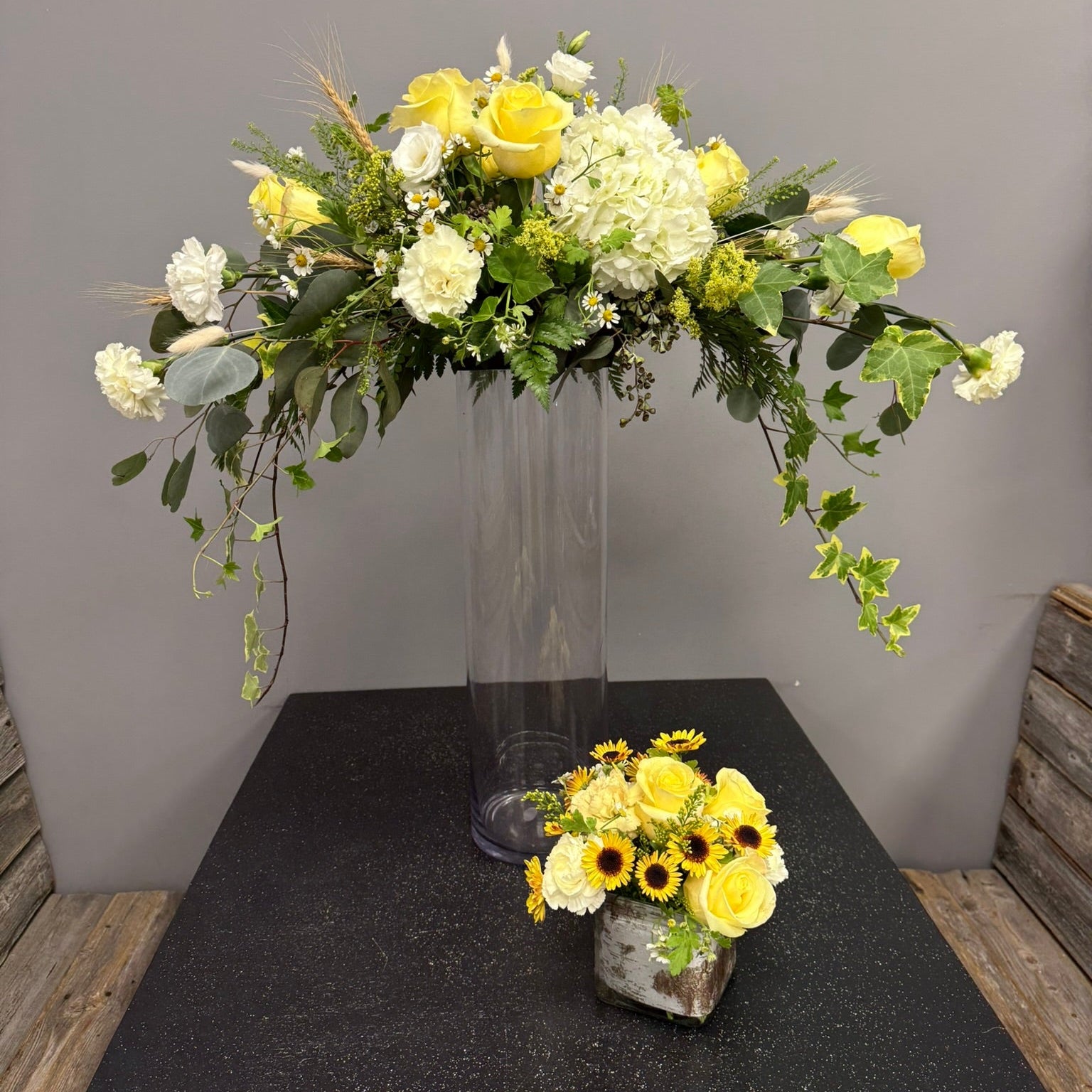 Floral arrangement in a tall glass vase on a dark surface with a gray background