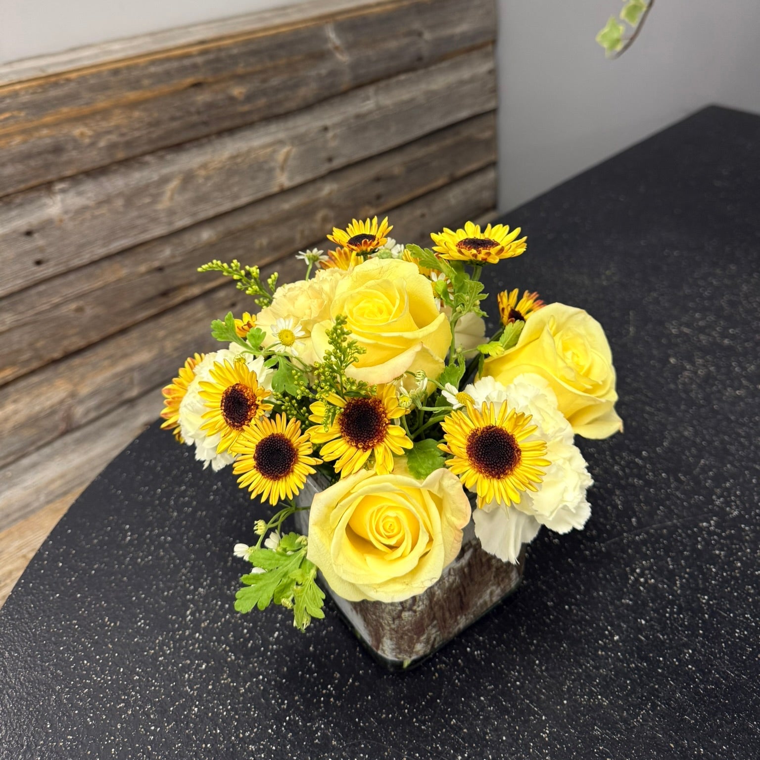 Floral arrangement with yellow flowers and sunflowers on a dark surface.