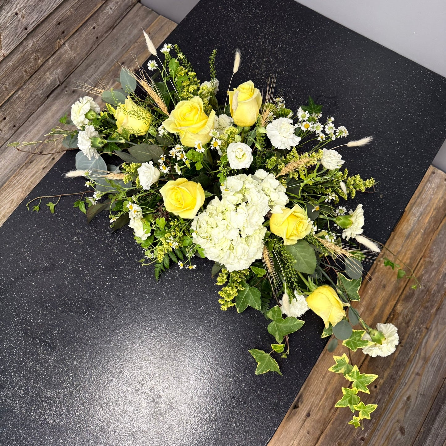 Bouquet of yellow and white flowers on a dark surface with wooden sides.