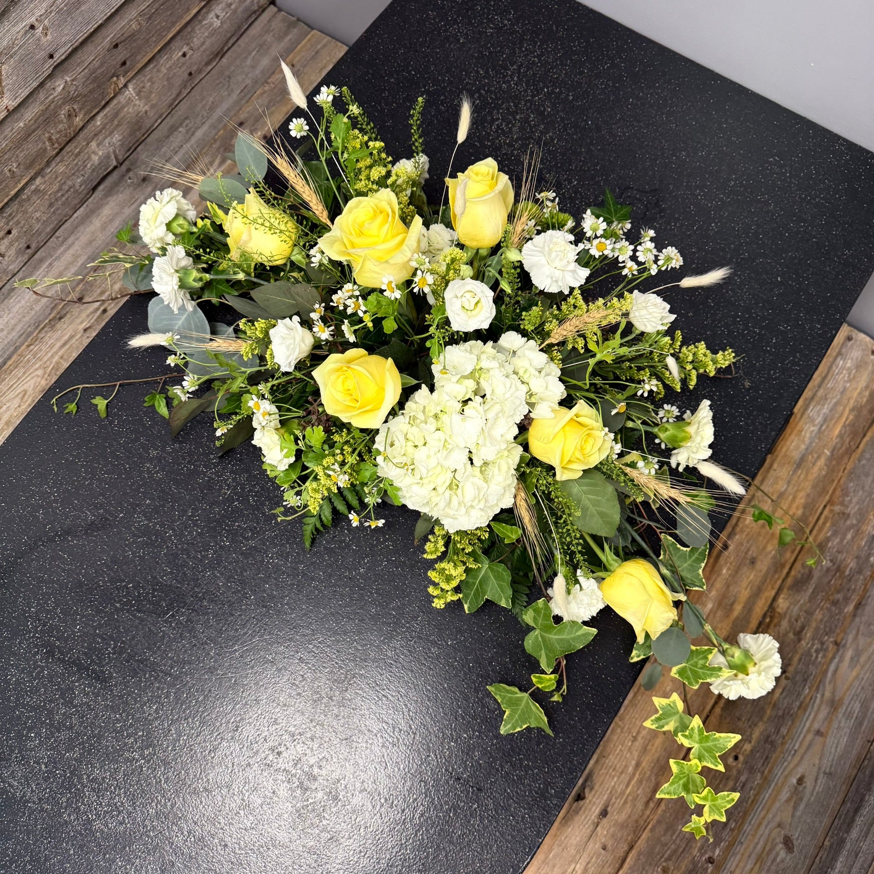 Bouquet of yellow and white flowers on a dark surface with wooden sides.