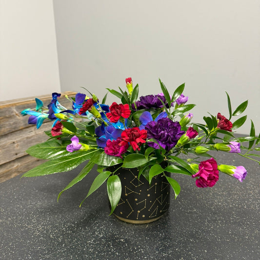Colorful flower arrangement in a black vase on a gray surface with a white wall background