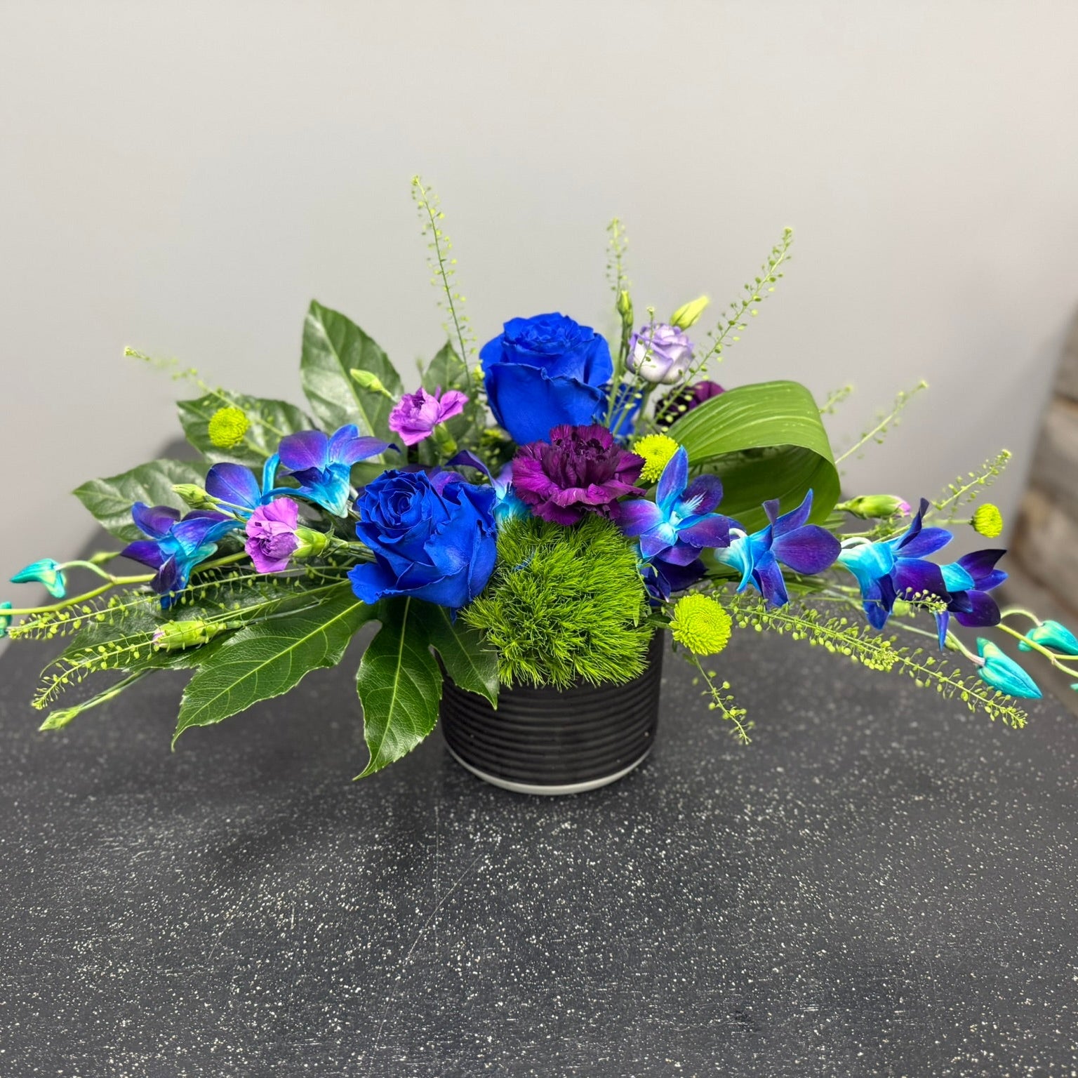 Floral arrangement with blue and purple flowers in a black pot on a gray surface.