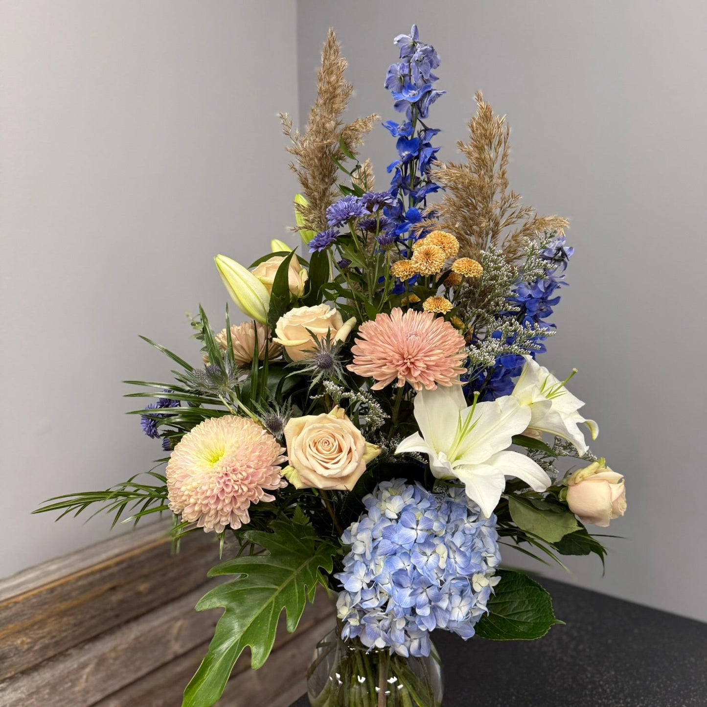 Bouquet of flowers in a clear vase on a dark surface with a gray background
