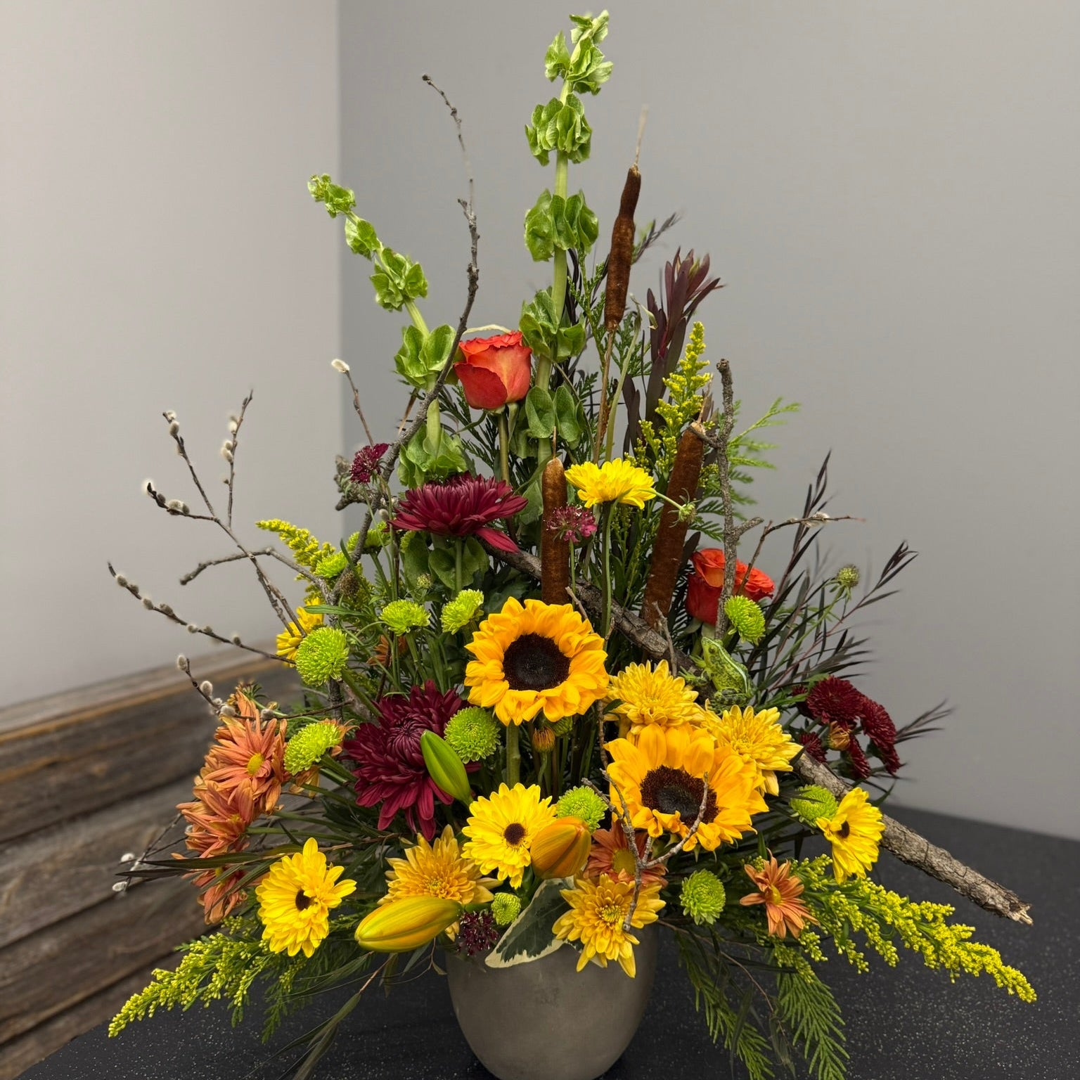 Floral arrangement with sunflowers and other flowers in a vase on a dark surface.
