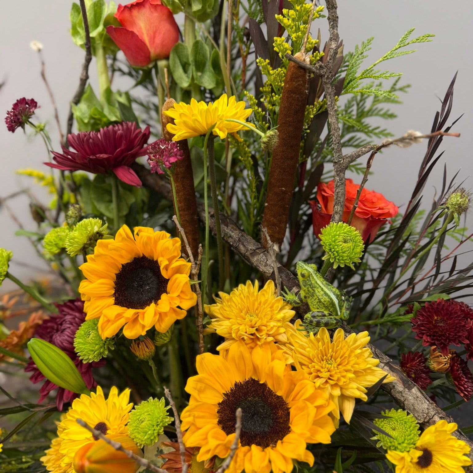 Bouquet of flowers with sunflowers, chrysanthemums, and other assorted flowers against a neutral background.